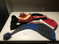 Assorted winter hats including black pom-pom beanie, multicolored knit hat, black and red hat, red knit hat, and grey-blue long knit hat with pom-pom tassel.