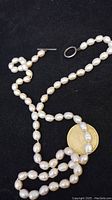 Full view of the 25-inch baroque pearl necklace laid out with a coin for scale, showing the unstamped metal toggle clasp and the irregular shapes of the pearls.