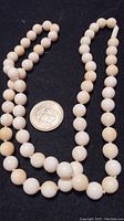 Knotted strand of round, white and cream natural beads approximately 1cm diameter, laid out with a coin for scale.