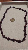 Full length of the garnet beaded necklace laid out with a coin for scale showing the entire strand and clasp.