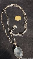Full view of the entire silver chain with pendant alongside a coin for scale to show length and size.