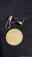 Close-up of one garnet earring placed beside a Canadian one dollar coin for size reference, showing the faceted garnet stone and sterling silver bezel setting.
