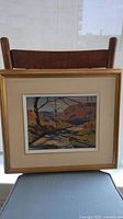 Framed landscape painting showing overall view on a chair.