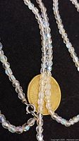Close-up photo showing the small facetted crystal beads strung together and the silver tone spring ring clasp, with a coin for size reference.
