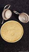 Pair of oval moonstone earrings next to a Canadian dollar coin for size reference on black background.