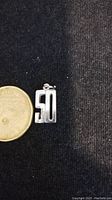 Front view of sterling silver number '50' charm next to Canadian quarter for scale.