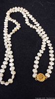 Full view of the 26 inch knotted sweet water pearl necklace against a black background, showing irregular shaped white pearls and a gold tone clasp.