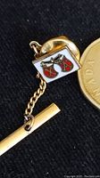 Close-up photo of the gold-tone tie pin with shield crest enamel design, chain, and bar, shown next to a Canadian coin for size scale.