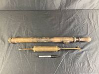 Two vintage brass hand pumps, one large and one smaller, displayed on a dark cloth background with a pen for scale.