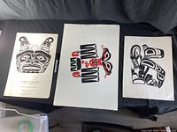 Three First Nation prints laid out flat on a black cloth, showing the overall condition and design of each print.