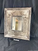 Full view of the framed mirror showing the carved tribal figures on the wooden frame and mirror surface reflecting part of an interior.