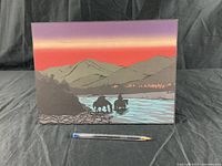 Front view of Indigenous artist print mounted on board showing two horse riders crossing a river with mountains and trees in the background. A pen placed in front for scale.