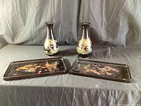 Full view of two black lacquer vases with dragon artwork and two matching rectangular trays with dragon designs on black lacquer background, set on black fabric