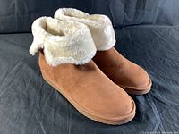 Side and angle view of brown Ugg style boot with cream faux fur cuff showing the exterior material and shape of the boot.