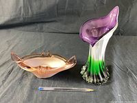 Pair of vintage glass sculptures including a pink oval bowl and a purple-green fluted vase with pen for scale.