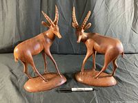 Front and right side view of both carved wooden antelope sculptures next to a marker for size reference.