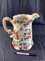 Front-side view of porcelain floral pitcher with shaped handle and gold trim