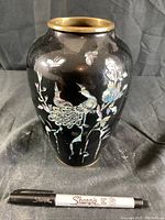 Front view of black metal vase showing detailed shell inlay of birds, flowers and butterflies with some wear and loss of color.