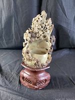 Front view of soapstone carving showing bird and flowers on wooden pedestal against black backdrop