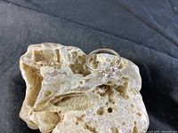 Ring placed on a textured piece of beige porous material with a black fabric background, showcasing the front view of the ring and stone.