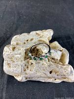 Ring placed on porous light stone showing top view with green stones visible