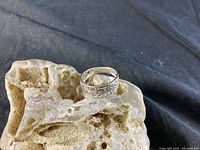 Silver ring shown resting on textured stone to highlight carved floral or geometric pattern around band.