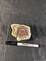 Tibetan turquoise and coral prayer box pendant placed on beige stone with black Sharpie marker for size reference.