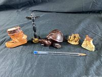 Photo showing five vintage collectible items: a carved wooden turtle, black totem pole, two ceramic miniature boots, and a small animal figurine. Pen included for size reference.