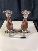 Pair of vintage metal candlestick holders side by side on a white surface with a black background. Both have ribbed, bulbous bodies and ornate tripod bases, with decorative tops showing floral and scroll details.