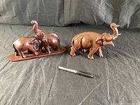 Three small wooden elephant figures on wood base and single large carved wooden elephant figure with pen for scale