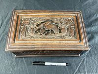 Top view of the closed wooden box showcasing detailed bird and floral carvings on the lid with a Sharpie marker for scale.