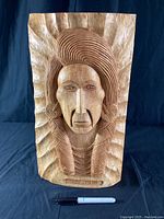 Full view of the wooden carved plaque showing Chief Joseph's head and upper torso with a sunburst background and a black pen for scale.