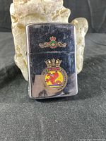 Front view of the Zippo lighter showing the Okanagan emblem with a crown and a red dragon on a yellow background.