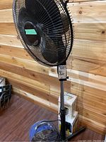 Black standing floor fan shown with protective metal grille, labeled dimensions 23x52.5 inches