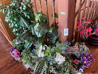 Overall group of faux plants and flowers arranged on floor and table showing variety of pots and flower types.
