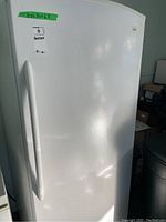 Front exterior view showing white upright freezer with handle and label.