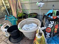 Wide view of garden pots, watering cans, soil bags, and plant trellis outside on a brick patio.