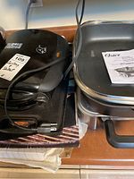 Side-by-side view showing the black Lagostina cast iron grill stacked near the Oster electric skillet with black cooking surface and handles.