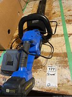 Photo showing entire hedge trimmer including handle, battery, and charger on wooden floor.
