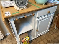 Overall front angle view of the kitchen island showing drawer, open shelf with three wooden knobs, cabinet door, and drop leaf on side.