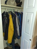 Closet view showing men's outerwear including a yellow raincoat, denim vest, and multiple shirts in various colors and patterns on hangers.