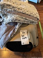 Small plastic pet crate with a beige faux fur blanket stacked on top of it, showing crate handle and part of door grille.