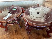Two wooden planter holders on floor showing circular tops and curved legs.