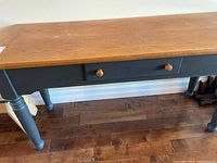 Full side view of the Palliser wooden side table showing painted legs and wooden top surface with drawer in middle.