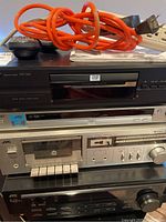 Stacked audio components showing Pioneer DV-343 DVD player on top, silver JVC cassette deck below, with orange power cord and remote on top.