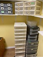 Tall white tower storage unit with multiple drawers and various smaller drawer units next to it on the left and stacked on the right side under shelf