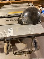 Front view of Mastercraft table saw on folding stand with wheels and black safety helmet (not included) placed on top