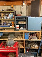 Photo showing shelves with motor, metal rods, tools including chisels and grinder wheels, housed in a basement workshop environment.