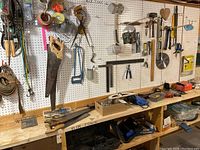 Workbench with various hand tools including a large hand saw, hammers, squares, and mounted pegboard with tools hanging
