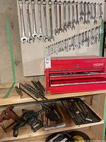 Metric wrenches mounted on board above red toolbox, with auger bits on shelf below
